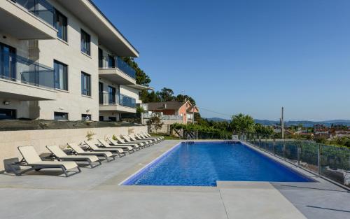 einen Pool mit Liegestühlen neben einem Gebäude in der Unterkunft Apartamentos Onzamar in Sanxenxo