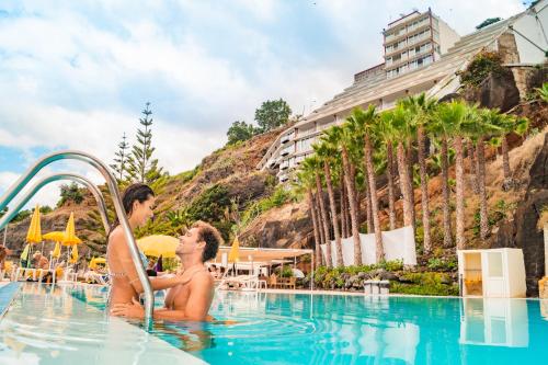 dos personas en una piscina en un complejo en Hotel Orca Praia, en Funchal