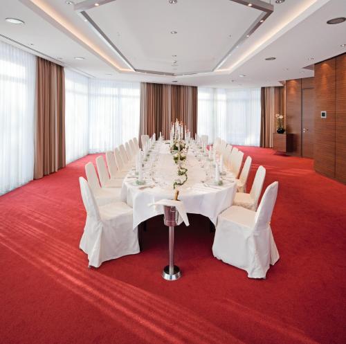 a conference room with a long table and white chairs at Mövenpick Hotel Münster am Aasee in Münster