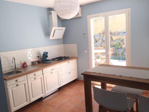 une cuisine avec des armoires blanches, une table et une fenêtre dans l'établissement L’oustau, à Rochefort-du-Gard