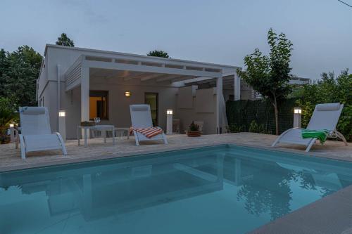 a swimming pool with chairs and a table and a house at Palms Villa in Scopello