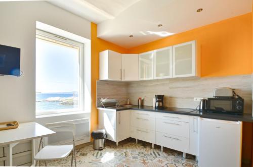 - une cuisine avec des placards blancs et un mur orange dans l'établissement Le petit Malmousque, à Marseille