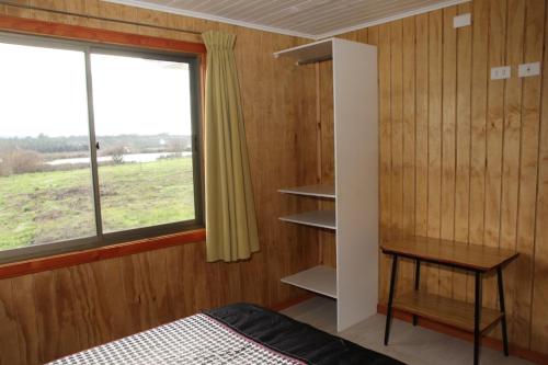 1 dormitorio con cama, ventana y mesa en Laguna Verde Cabaña, en Nueva Imperial