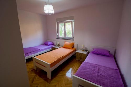 duas camas num pequeno quarto com lençóis roxos em Apartman Vitina em Ljubuski