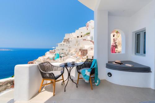 a balcony with a table and chairs overlooking the ocean at ArmonOia Luxury Caves in Oia