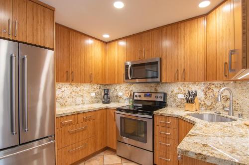a kitchen with wooden cabinets and a stainless steel refrigerator at Nāpili Surf Beach Resort by Castle in Lahaina