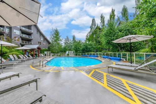 a swimming pool with benches and an umbrella at The Best Top Floor Ski-in/Ski-out at the Aspens in Whistler