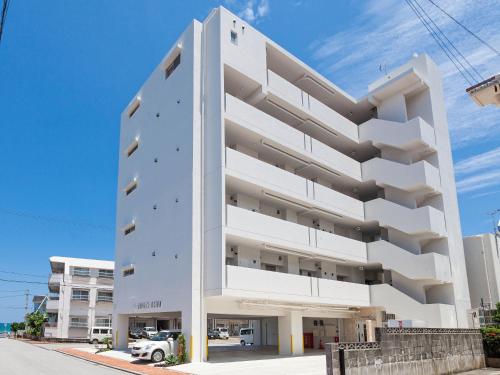 a white building on a street with a blue sky at Yonabaru Hotel SUNRIZE OCEAN in Yonabaru