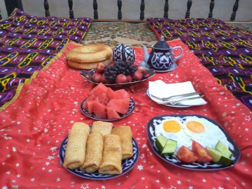 a table with plates of breakfast food on a red table cloth at Zafar Family Guesthouse in Bukhara