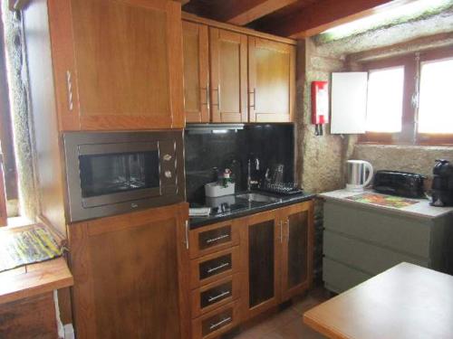 a kitchen with wooden cabinets and a sink and a microwave at Casa do Forno in Almeida