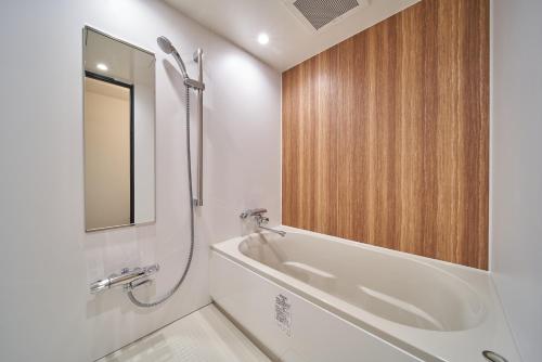 a white bathroom with a tub and a mirror at cinnamon hotel in Osaka