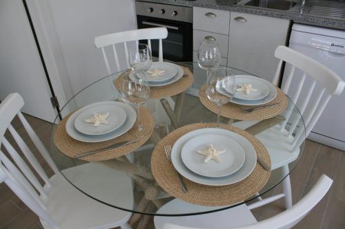 a glass table with white chairs and plates and glasses at Recantus Comporta in Comporta