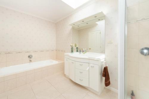 a white bathroom with a sink and a tub and a mirror at TAURANGA CITY CBD 5TH AVE Elegant Entire Home in Tauranga