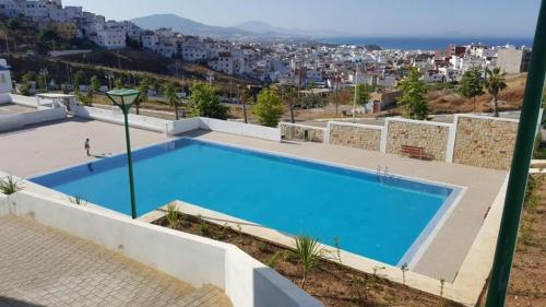 a large blue swimming pool with a city in the background at Résidence Lilia Al Jabal M’diQ in M'diq