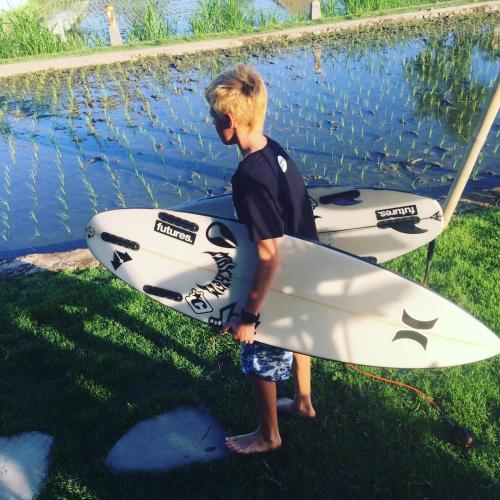a young boy holding a surfboard next to a body of water at Padi guest house in Keramas