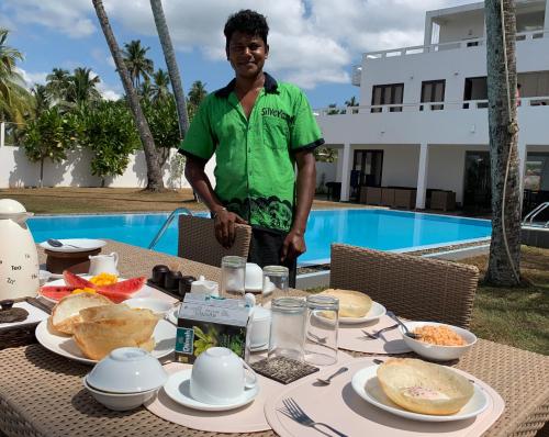Um homem em pé em frente a uma mesa com comida. em Silverlane Beach House em Matara