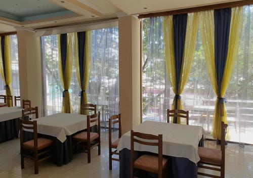 a dining room with two tables and chairs and large windows at Hotel Palma in Durrës