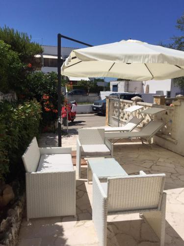 a group of white chairs and an umbrella at 21mq Home Petrolla in Villanova di Ostuni