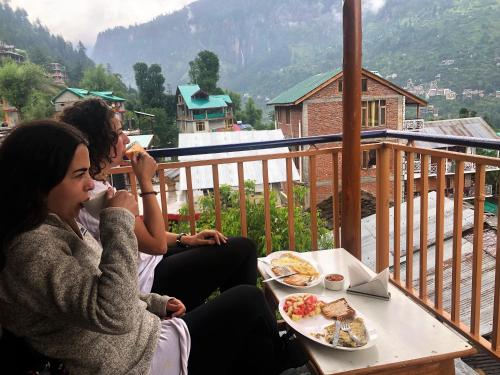 two women sitting at a table eating food on a balcony at La Voglia-Old Manali in Manāli