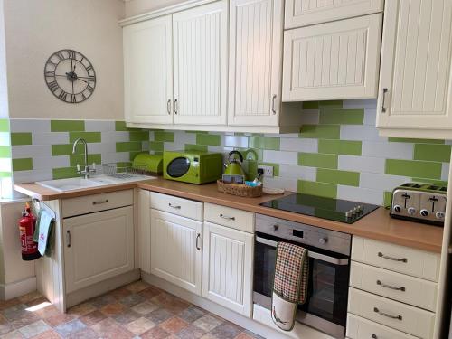 uma cozinha com armários brancos e azulejos verdes e brancos em Postmans Rest, second floor apartment, Lynmouth with private parking em Lynmouth