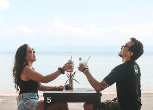 a man and woman sitting at a table on the beach with drinks at Tiki Beach Koh Phangan Beach Restaurant Bar and Coworking in Ban Tai