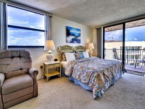 a bedroom with a bed and a chair and windows at Madeira Towers 601 Beach front with spectacular views 533 in St Pete Beach