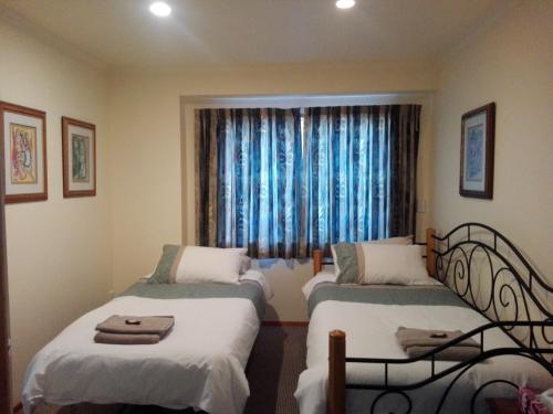 ニュープリマスにあるTaranaki Experienceのベッド2台、青いカーテン付きの窓が備わる客室です。