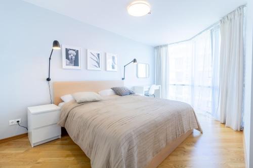 a white bedroom with a bed and a large window at Elija Swan-Toy Apartments in Šventoji