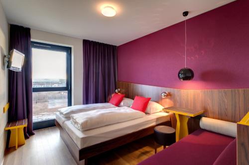 Habitación de hotel con cama y pared púrpura en MEININGER Hotel Frankfurt Main / Airport, en Frankfurt