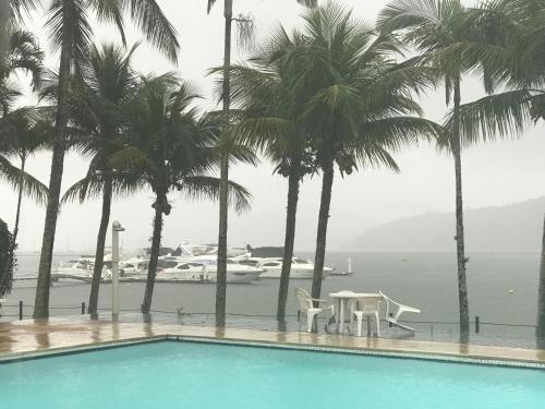 a swimming pool with palm trees and a boat in the water at Confortável Casa Condomínio Marbella in Angra dos Reis