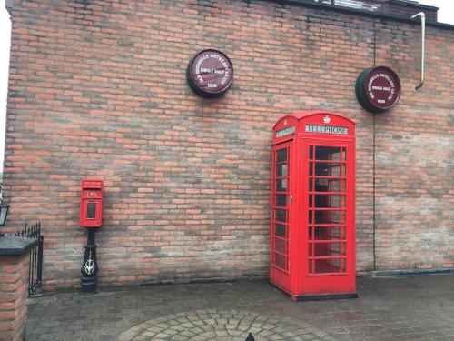 a brick wall with two red phone booths and a clock at Bush House Accommodation - The Distillery in Bushmills