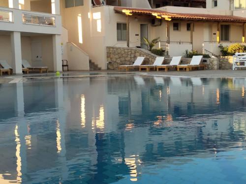 a pool in front of a building with white chairs at Creta Suites in Koutsounari