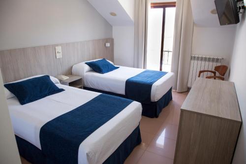 um quarto de hotel com duas camas com lençóis azuis e brancos em Hotel Restaurante Glasgow em Villadesuso