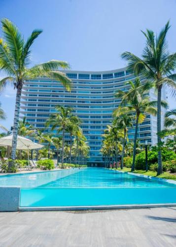 a swimming pool in front of a tall building with palm trees at PENINISULA ViSTA AL MAR BY ENNA INN IXTAPA in Ixtapa
