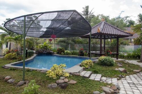 einen Pool im Garten mit einem Sonnenschirm und einem Tisch in der Unterkunft RedDoorz Syariah Plus near Banyuwangi Airport in Dadapan