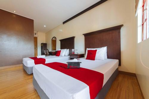 two beds in a hotel room with red and white sheets at RedDoorz Plus @ Starhomes Olivianville in Tarlac
