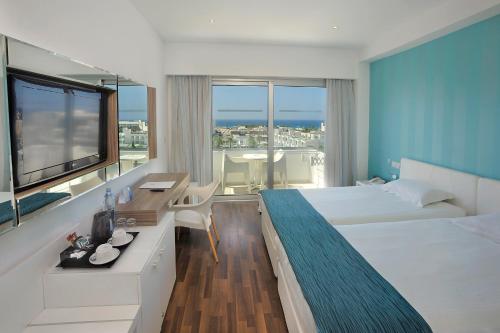 a hotel room with a bed and a desk and a large window at Nestor Hotel in Ayia Napa