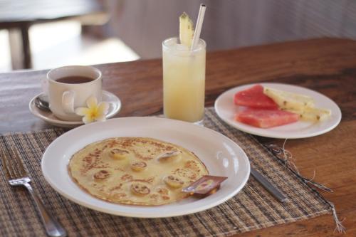 a table with two plates of food and a glass of orange juice at D'Muncuk Huts Lembongan in Nusa Lembongan
