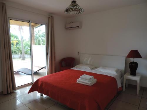 1 dormitorio con 1 cama con manta roja y ventana en Villas Manapany, en Saint-Joseph