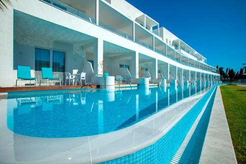 a swimming pool next to a building with blue chairs at Aliathon Aegean in Paphos City
