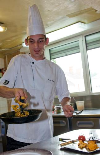 a chef in a kitchen holding a plate of food at Logis Auberge Du Centre in Chitenay
