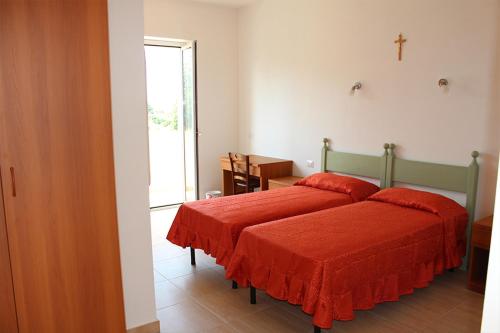 Cette chambre comprend un lit avec des draps rouges et une croix sur le mur. dans l'établissement Oasi di Pace, à Sutri