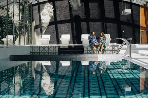 two women sitting on a bench next to a swimming pool at City Park Hotel & Residence in Poznań