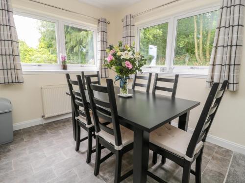 a dining room with a black table and chairs and windows at Falla Farmhouse in Jedburgh