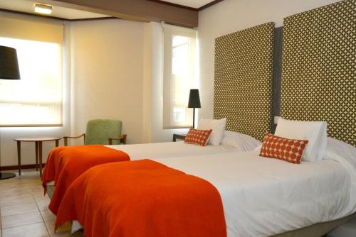 two beds in a hotel room with orange sheets at Hotel ACA El Calafate in El Calafate
