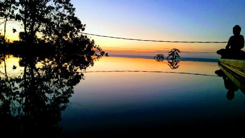 a person sitting next to a body of water at sunset at Cantik Villa in Lovina