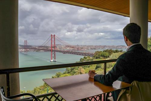 a man sitting at a table with a view of the golden gate bridge at HI Almada - Pousada de Juventude in Almada
