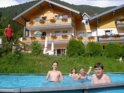 a group of people in a swimming pool in front of a house at Hotel Hammerwirt - Forellenhof in Untertauern
