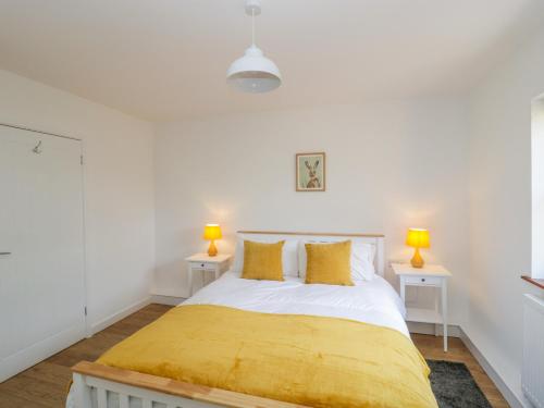 a white bedroom with a bed with yellow sheets and two tables at Mendip Cottage in Shipham