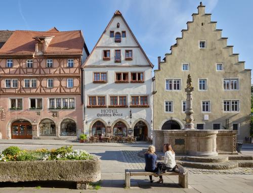 dos mujeres sentadas en un banco frente a los edificios en Historik Hotel Gotisches Haus garni, en Rothenburg ob der Tauber